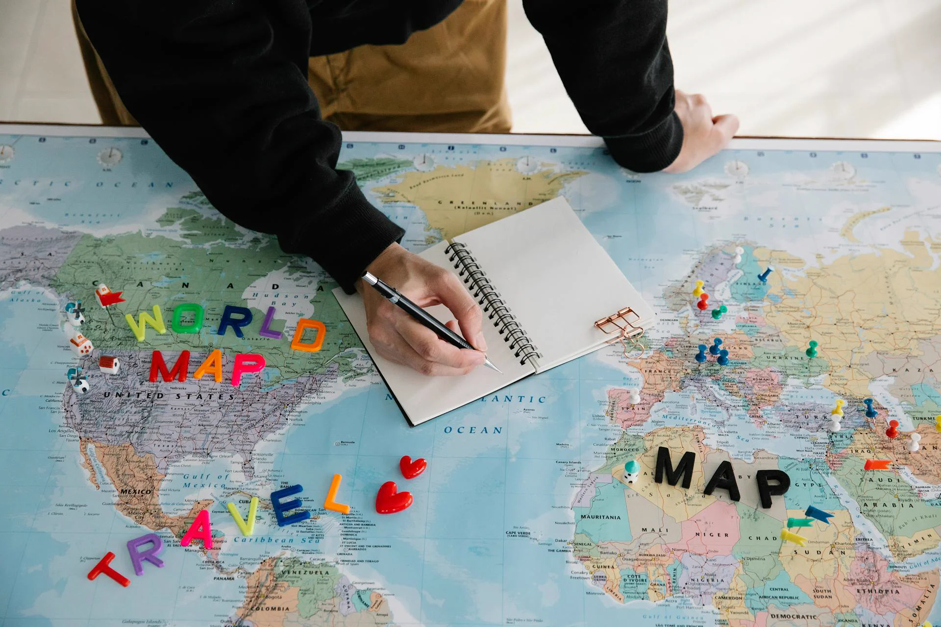 Person planning a journey on a world map with notebook and markers